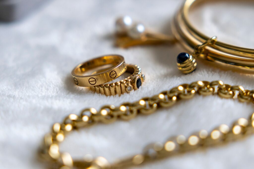 Collection of gold rings, bracelets, and chains with gemstones on a textured surface.